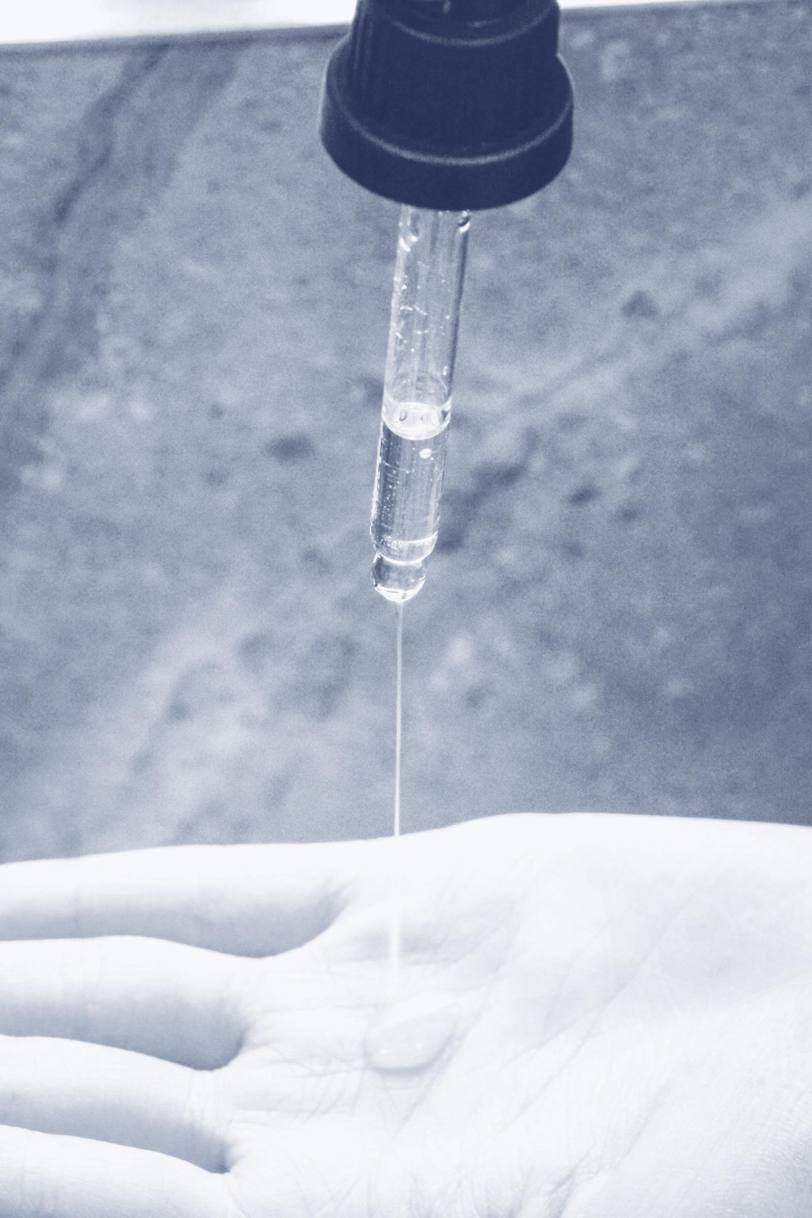 A dropper releasing a clear serum onto a palm